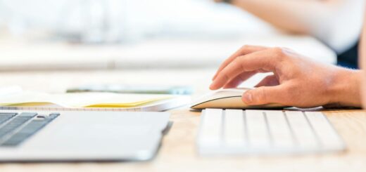 A person working at a laptop with a wireless mouse and keyboard in a bright office setting.