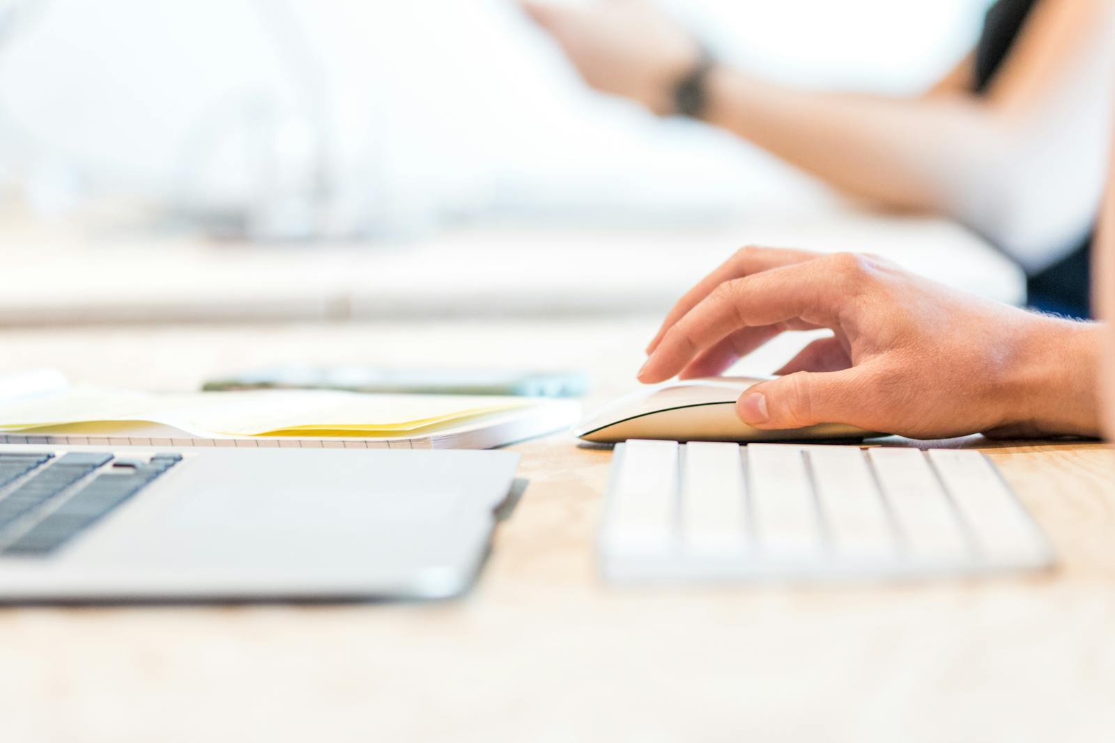 A person working at a laptop with a wireless mouse and keyboard in a bright office setting.